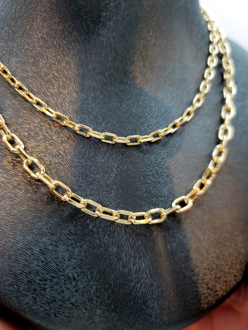 Puede incluir: Un collar de cadena en tono dorado con eslabones rectangulares alargados. La cadena est&aacute; dispuesta en capas, mostrando dos hilos distintos con el mismo dise&ntilde;o de eslabones de metal pulido, creando un aspecto uniforme y brillante.
