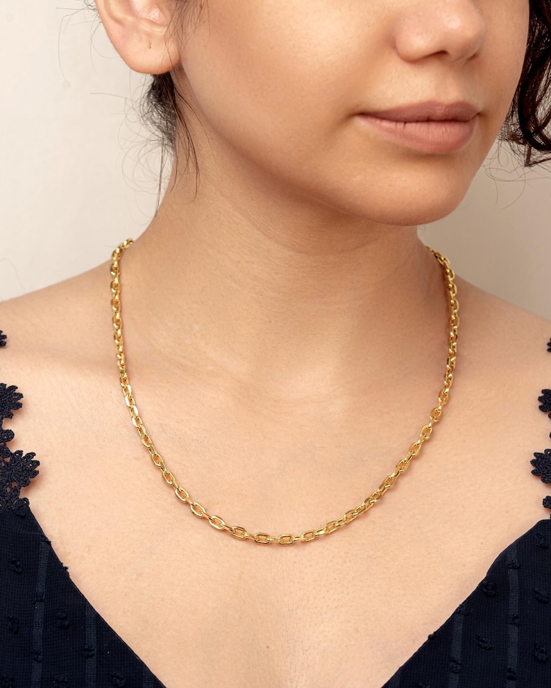 Puede incluir: Un collar de cadena en tono dorado que presenta una serie de eslabones uniformes de forma ovalada. El collar descansa sobre el cuello, mostrando un acabado met&aacute;lico pulido y reflectante que capta la luz, creando un patr&oacute;n de eslabones cl&aacute;sico.