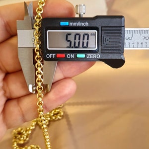 May include: Close-up of a gold chain measured with a digital caliper. The caliper reads 5.00 mm.