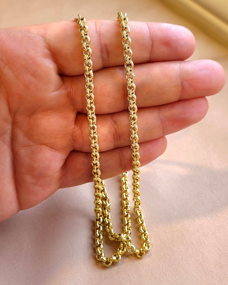 May include: A gold chain necklace with a delicate, rounded link design. The chain is shown lying on a hand, with the ends of the chain overlapping.