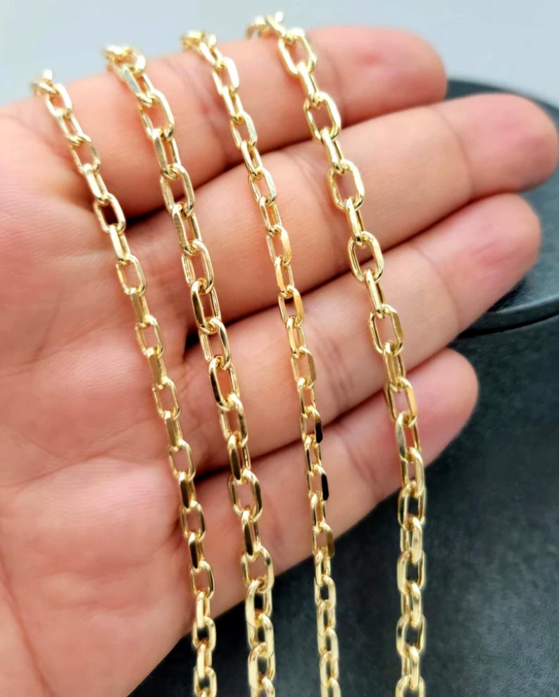Puede incluir: Un collar de cadena de oro que presenta una serie de eslabones ovalados alargados y uniformes conectados en un patr&oacute;n continuo. El metal tiene una superficie pulida y reflectante que capta la luz, creando un aspecto amarillo met&aacute;lico.