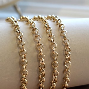 May include: Four gold chains, each with a delicate, round link pattern, are arranged in a stack on a white surface. The chains are all the same length and width, and they are all made of a shiny, polished gold.