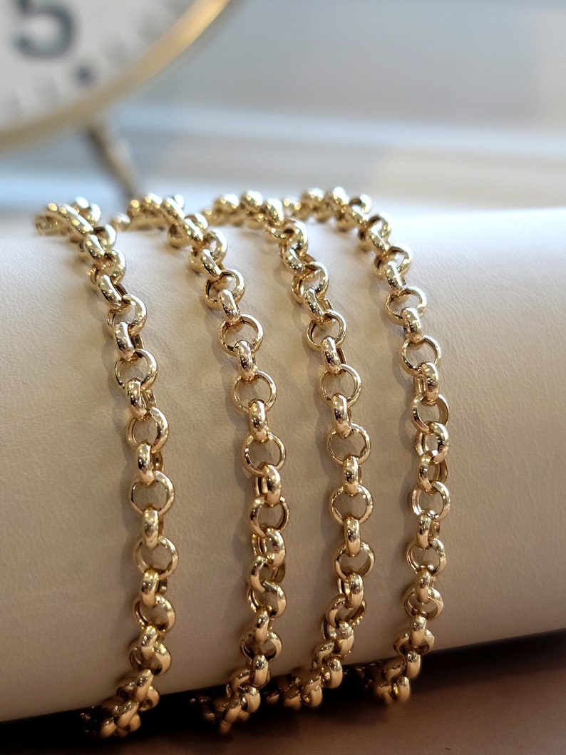 May include: Four gold chains, each with a delicate, round link pattern, are arranged in a stack on a white surface. The chains are all the same length and width, and they are all made of a shiny, polished gold.