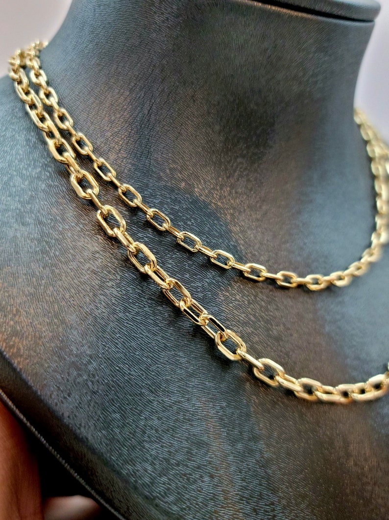 Puede incluir: Un collar de cadena en tono dorado que presenta una serie de eslabones ovalados y alargados conectados en un patr&oacute;n continuo y uniforme. La superficie met&aacute;lica tiene un acabado pulido y reflectante que capta la luz, resaltando los eslabones.