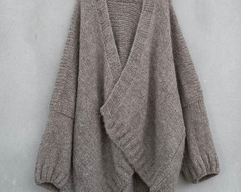 May include: A brown knitted cardigan with a deep V-neck and long sleeves. The cardigan is draped over a hanger and has a relaxed fit.