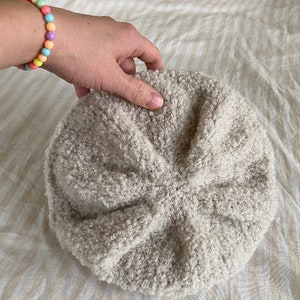 May include: A beige fuzzy beret with a soft, textured surface.