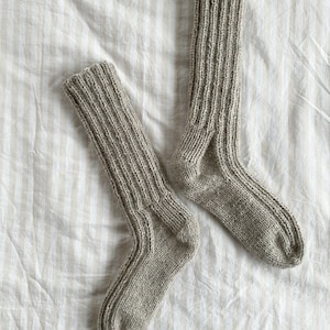 May include: A pair of grey knitted socks on a white and beige striped fabric background.