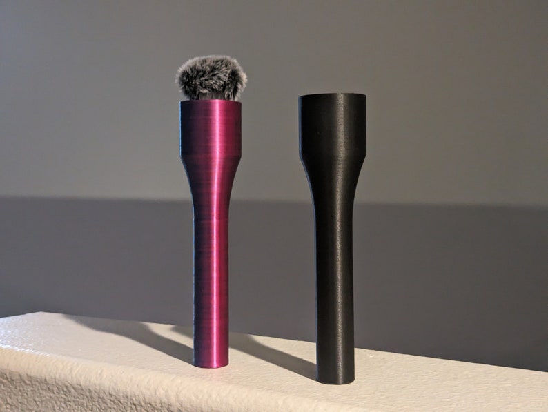May include: Two microphone accessories. One is a deep magenta color with a fuzzy, gray microphone cover. The other is a matte black color. Both have a cylindrical shape with a flared base.