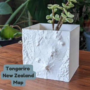 Puede incluir: Maceta de cerámica blanca con forma de mapa 3D de Tongariro, Nueva Zelanda. La maceta tiene una pequeña planta verde en su interior.