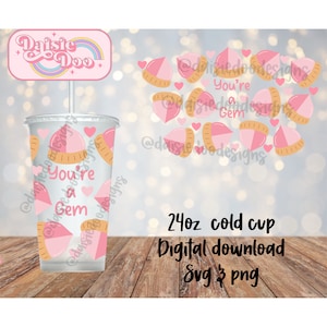 May include: A pink and gold 24 ounce cold cup with a design of pink and gold hearts and the text "You're a Gem". The cup is on a wooden surface. The text "Daisie Doo" is on a pink and gold banner with a rainbow.