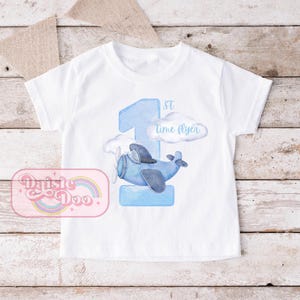Könnte beinhalten: Weißes T-Shirt mit einer blauen Aquarell-Eins, einem blauen Flugzeug und dem Text "1st time flyer".