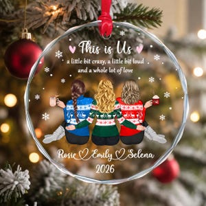 May include: A round, clear acrylic Christmas ornament featuring an illustration of three people from behind, wearing patterned sweaters. Text reads: This is Us, a little bit crazy, a little bit loud and a whole lot of love, Rosie, Emily, Selena, 2026.