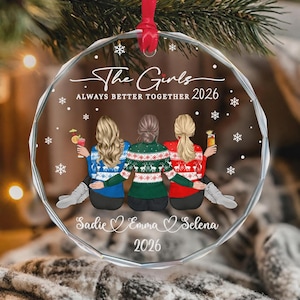 May include: A clear, circular acrylic ornament featuring a printed illustration of three people from behind, wearing festive sweaters. The text reads "The Girls ALWAYS BETTER TOGETHER 2026" and "Sadie Emma Selena 2026" with snowflake accents.