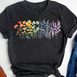 May include: A dark grey t-shirt with a rainbow floral print. The flowers are arranged in a horizontal line across the front of the shirt.