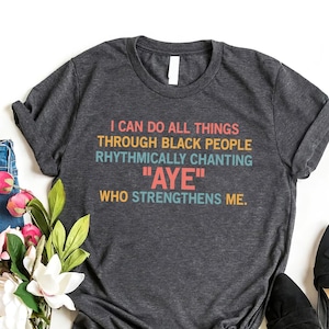 May include: A dark heather grey t-shirt with a white, black, and rainbow colored graphic print that reads "I can do all things through black people rhythmically chanting "AYE" who strengthens me."