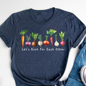 May include: A navy blue t-shirt with a graphic of various vegetables and the text "Let's Root For Each Other".