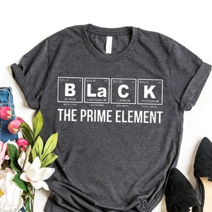 May include: A dark grey t-shirt with a white graphic design featuring the periodic table elements for Boron, Lanthanum, Carbon, and Potassium, spelling out the word "BLACK". The text "THE PRIME ELEMENT" is printed below the graphic.