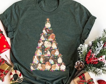 May include: A green t-shirt featuring a Christmas tree design made up of guinea pigs. The guinea pigs are wearing Santa hats and other festive accessories. The tree is decorated with colourful lights.