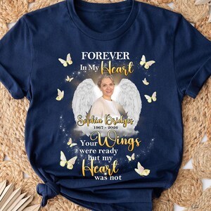 May include: Navy blue t-shirt with the text "FOREVER In My Heart" and "Your Wings were ready but my Heart was not." The shirt features a photo of a woman with angel wings and the name "Sophia Bridges 1967-2026" with butterfly graphics.