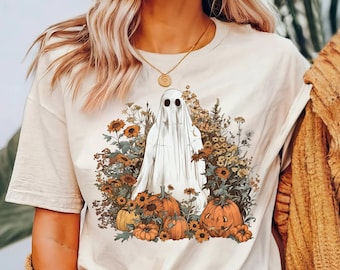 Op de afbeelding: Een beige T-shirt met een grafische print van een witte geest die in een veld met oranje pompoenen en gele bloemen staat.