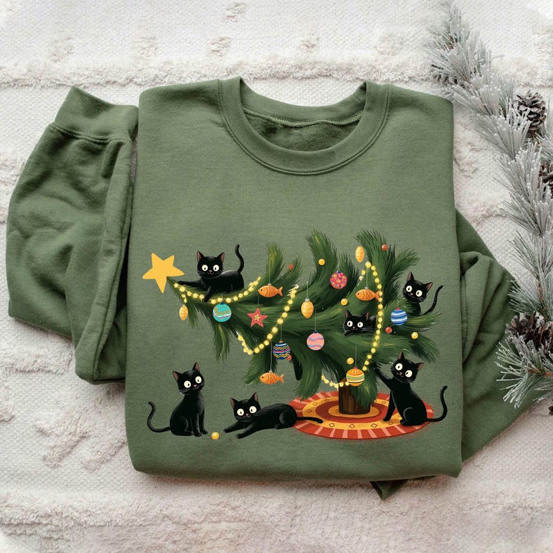 Op de afbeelding: Olijfgroene sweatshirt met een kerstboomontwerp. De boom is versierd met ballen en lichtjes, omringd door zwarte katten. De sweatshirt heeft een ronde hals en lange mouwen, perfect voor de wintermaanden.