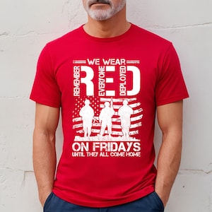 Può includere: Maglietta rossa con un design grafico bianco che dice "We Wear Red Everyone Deployed On Fridays Until They All Come Home". La grafica presenta anche tre soldati in piedi davanti a una bandiera americana.
