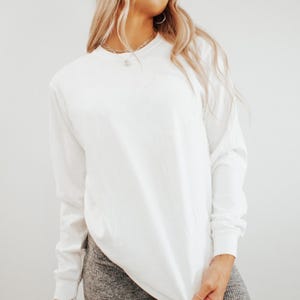 May include: A white long-sleeve shirt. The shirt has a crew neck and is made of a soft, opaque material. The sleeves are long and end at the wrists. The shirt is a solid white color.