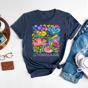 May include: A navy blue t-shirt with a colorful floral design and the text "Let Kindness Bloom".