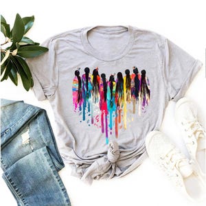 May include: A gray t-shirt with a colorful graphic of women standing in a heart shape. The graphic is made up of colorful paint splatters.