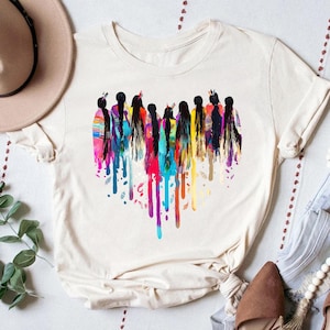 May include: A white t-shirt with a colorful graphic of a group of women with long hair. The women are painted in a watercolor style with dripping paint.