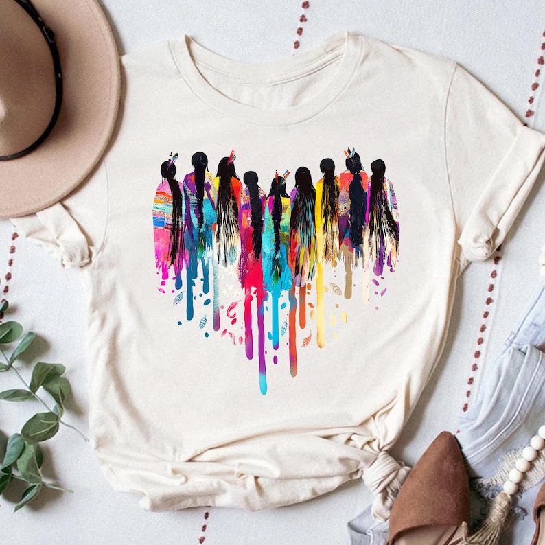 May include: A white t-shirt with a colorful graphic of a group of women with long hair. The women are painted in a watercolor style with dripping paint.