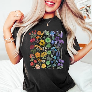 May include: A black t-shirt with a rainbow floral design. The flowers are arranged in a rainbow pattern, with red, orange, yellow, green, blue, indigo, and violet flowers.