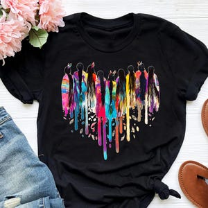May include: Black t-shirt with a colorful heart design featuring a group of women with long hair. The heart is made of dripping paint in various colors, including red, orange, yellow, green, blue, and purple.