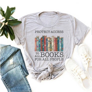 May include: Grey t-shirt with the text "Protect Access to All Books for All People" and a graphic of a stack of colourful books with floral designs.