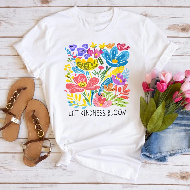 May include: White t-shirt with a colorful floral design and the text "Let Kindness Bloom".