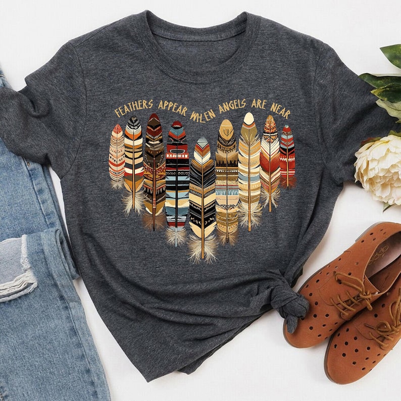 May include: A dark gray t-shirt with a graphic of colorful feathers and the text "Feathers appear when angels are near".
