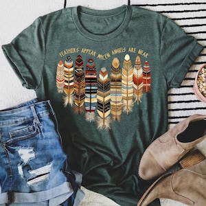 May include: Green t-shirt with a graphic of colorful feathers and the text "Feathers appear when angels are near".