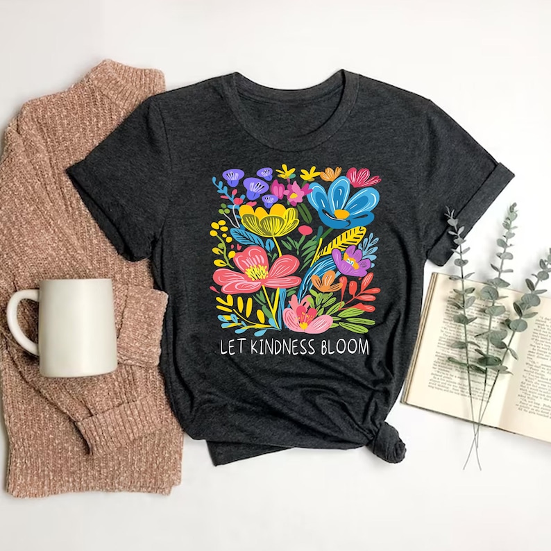 May include: A dark gray t-shirt with a colorful floral design and the text "Let Kindness Bloom".