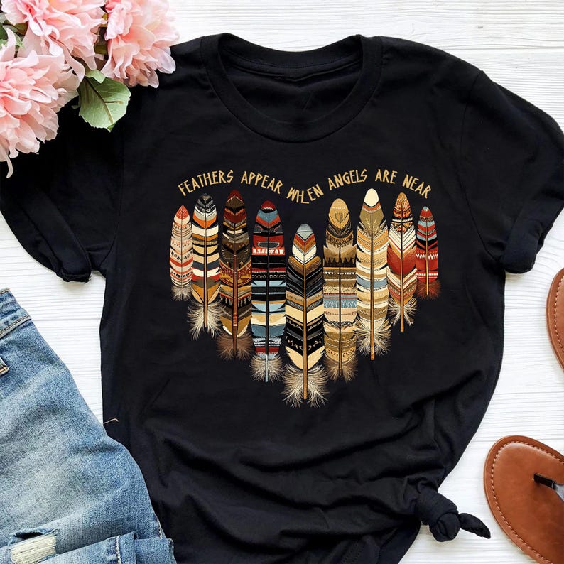 May include: Black t-shirt with a graphic of colorful feathers and the text "Feathers appear when angels are near".