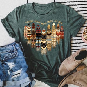 May include: Green t-shirt with a graphic of colorful feathers and the text "Feathers appear when angels are near".