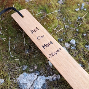 May include: Wooden bookmark with a black ribbon. The bookmark is engraved with the text "Just One More Chapter".