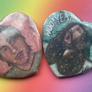 May include: Two heart-shaped buttons with glitter and text. The pink button features a person with white hair and the text "Sparkle On It's Wednesday". The green button features a person with long hair and the text "Woo! Yeah Baby!"