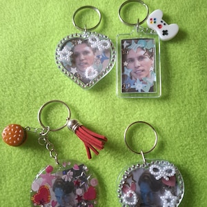 May include: Four keychains with different designs. One keychain features a heart-shaped resin charm with a photo inside, another has a rectangular resin charm with a photo inside, a third has a round resin charm with a photo inside, and the last has a heart-shaped resin charm with a photo inside and a small game controller charm.