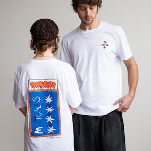 May include: Two people wearing white t-shirts with graphic designs. One shirt features a matchbox design on the back with the word "MATCHES" and stars. The other shirt has a match and stars design on the front. The shirts are paired with dark trousers.
