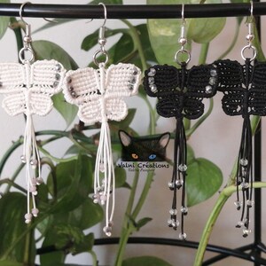 Peut inclure: Deux paires de boucles d'oreilles en forme de papillon, une paire est blanche avec des perles argentées et l'autre paire est noire avec des perles transparentes.