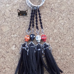 May include: A keychain with four black tassels and four skull beads in orange, black, and white. The keychain is attached to a set of silver rings.
