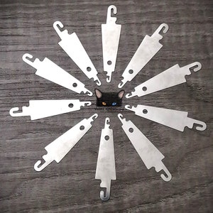 Peut inclure: Dix outils en métal argenté pour enfiler le fil disposés en cercle sur une surface en bois. Les enfile-aiguilles ont une petite boucle en haut et un petit trou au milieu.