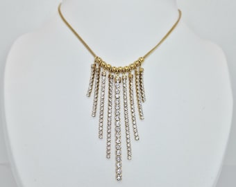 May include: A gold-toned necklace with a cascade of sparkling, clear gemstones. The necklace features a delicate chain and a series of vertical gemstone strands, creating a glamorous, eye-catching design. The necklace is displayed on a white mannequin.