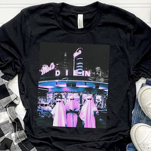 Op de afbeelding: Zwart T-shirt met een grafische print van een diner met de woorden "Mel's Diner" en twee figuren in witte gewaden die voor het diner staan.