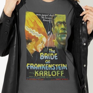 May include: A dark grey t-shirt with a vintage movie poster design featuring the Bride of Frankenstein. The poster features the text "The Bride of Frankenstein" and "Boris Karloff".